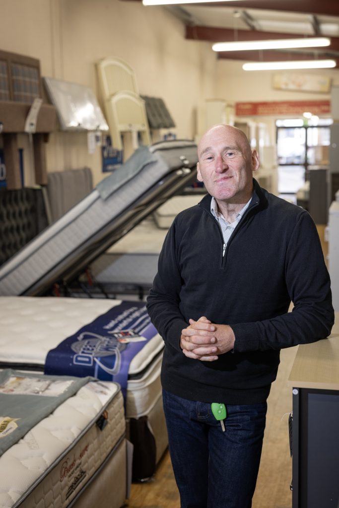 Man standing in a showroom filled with beds and mattresses.